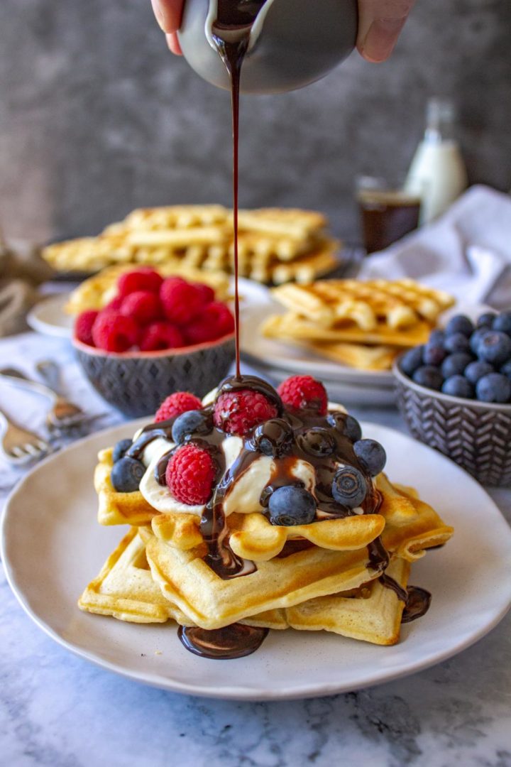 Waffles topped with cream, berries and chocolate sauce