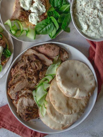 Roast leg of lamb carved and plated next to pitas.