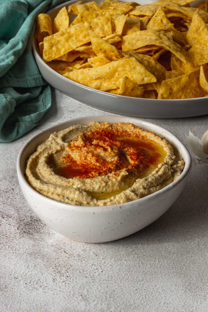 Simple Hummus in a bowl sprinkled with paprika next to a plate of chips