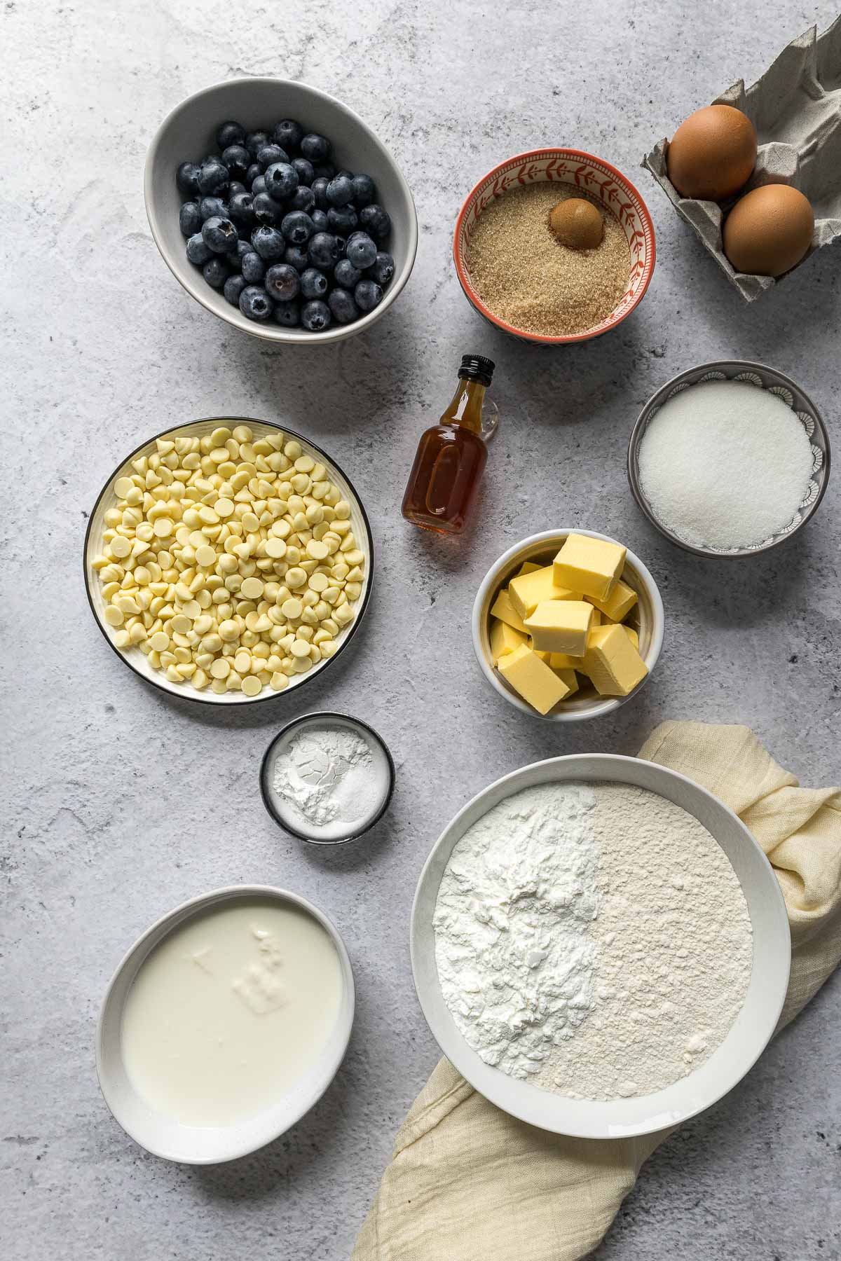 Blueberry muffin ingredients - sugar, flour, cornstarch, eggs, salt, baking powder, vanilla, yoghurt, milk, brown sugar and cinnamon, butter, white chocolate chips, blueberries