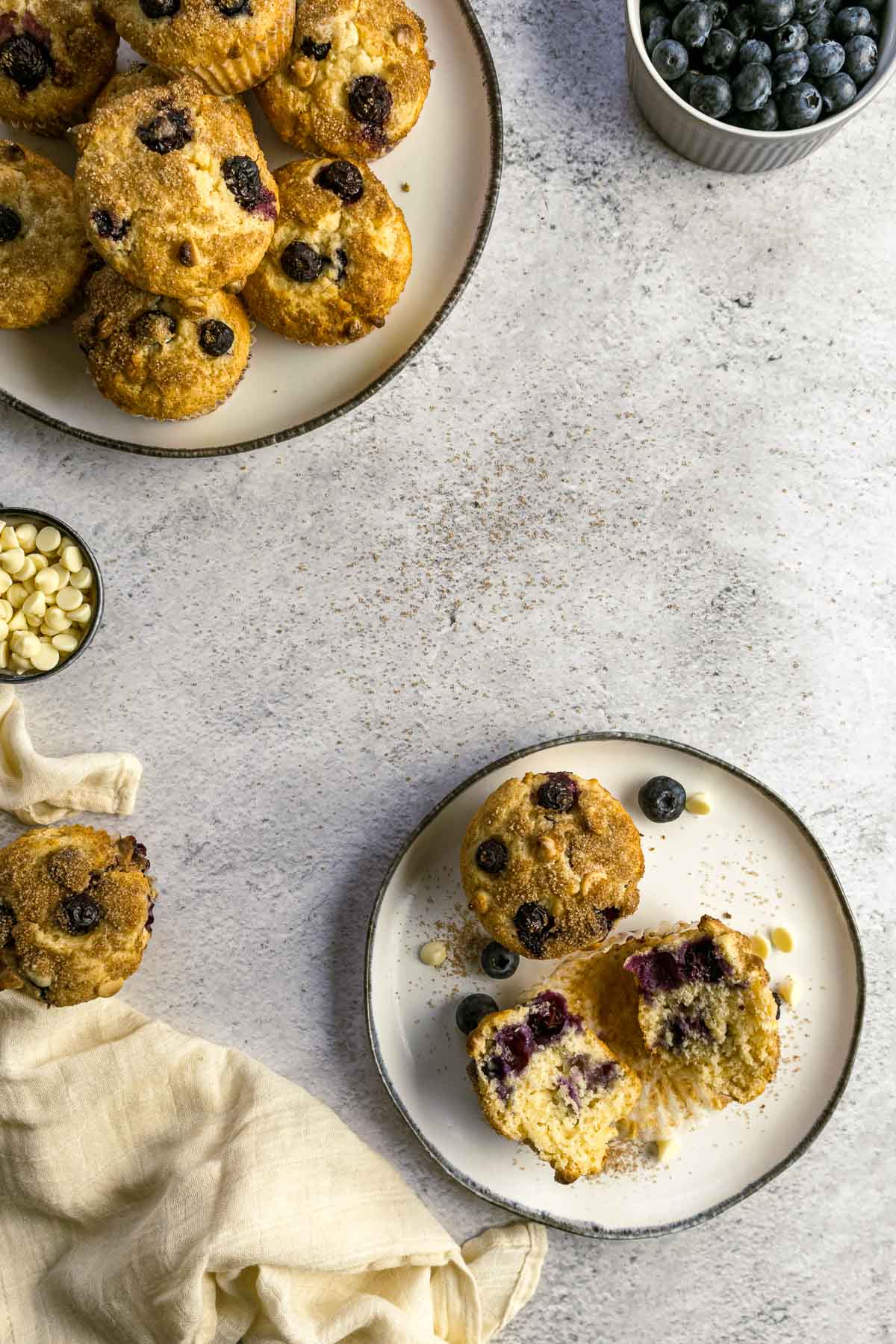 Blueberry muffin split in two on a plate with an extra muffin next to a plate of muffins