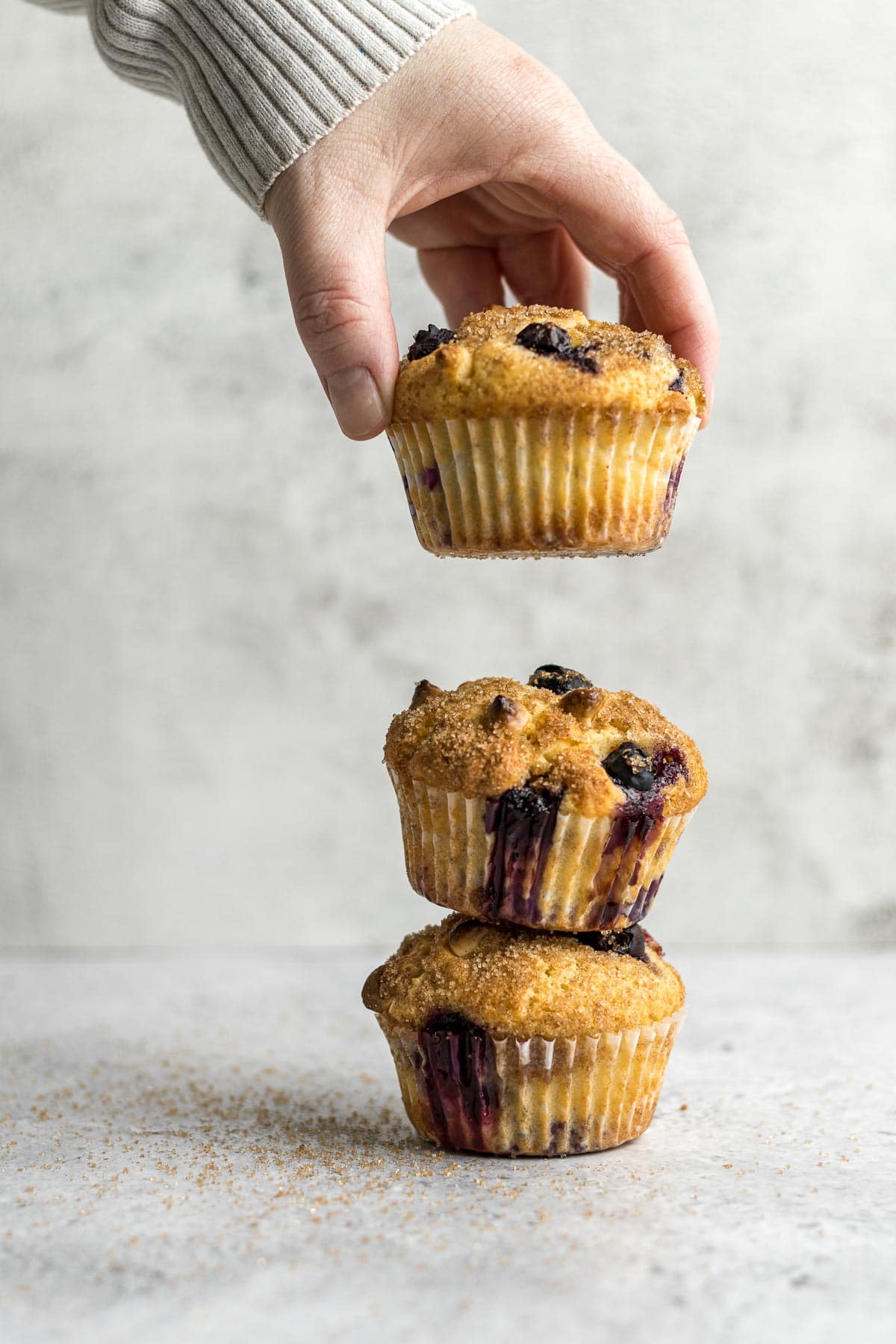 Blueberry muffins stacked on each other with a hand ready to place the third one of top.