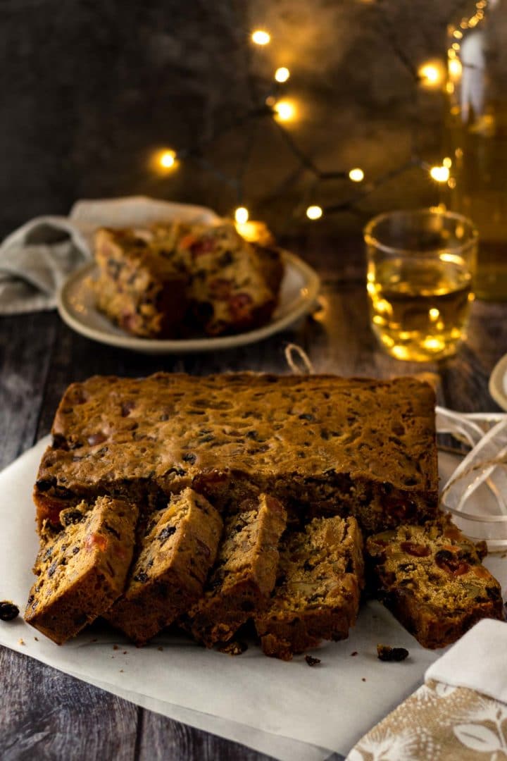 Sliced Christmas fuit cake with glass of brandy in the background.