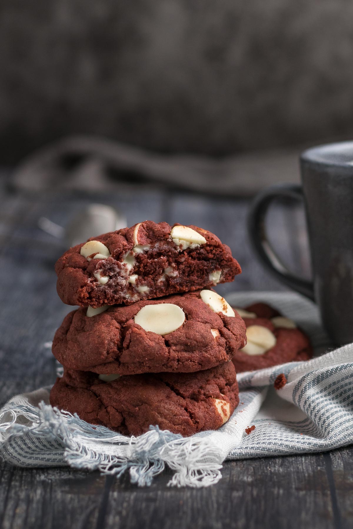 Stacked red velvet cookies next to a coffee cup.