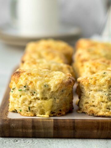 Close up of cheese and chives scones on a board with a cup in the background.