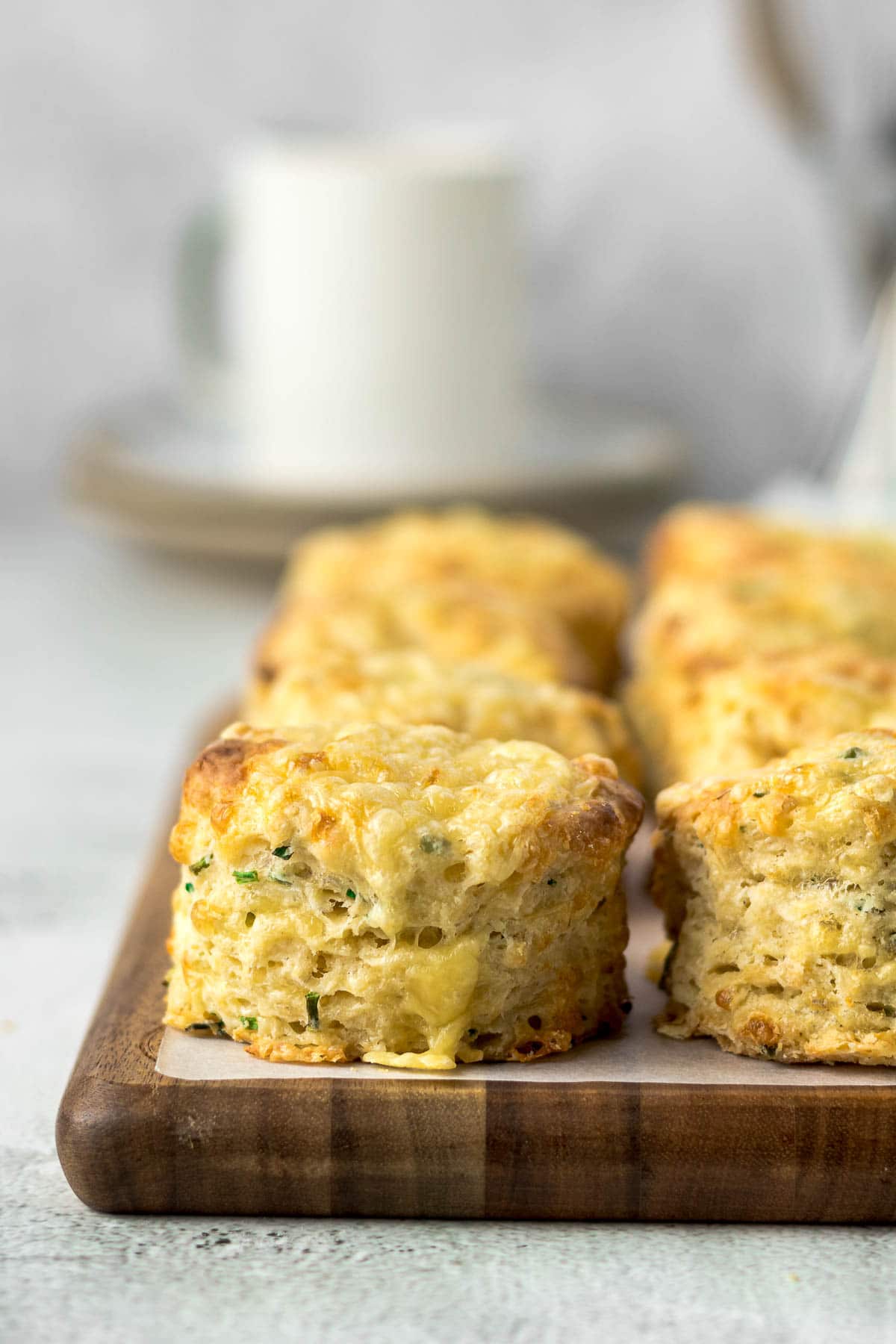 Close up of cheese and chives scones on a board with a cup in the background.