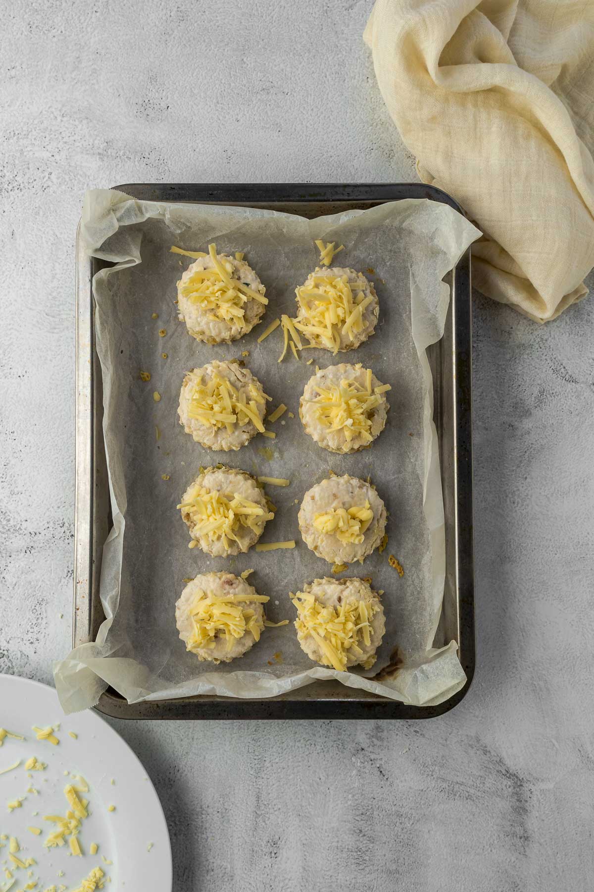 Scones on a baking tray topped with cheese.