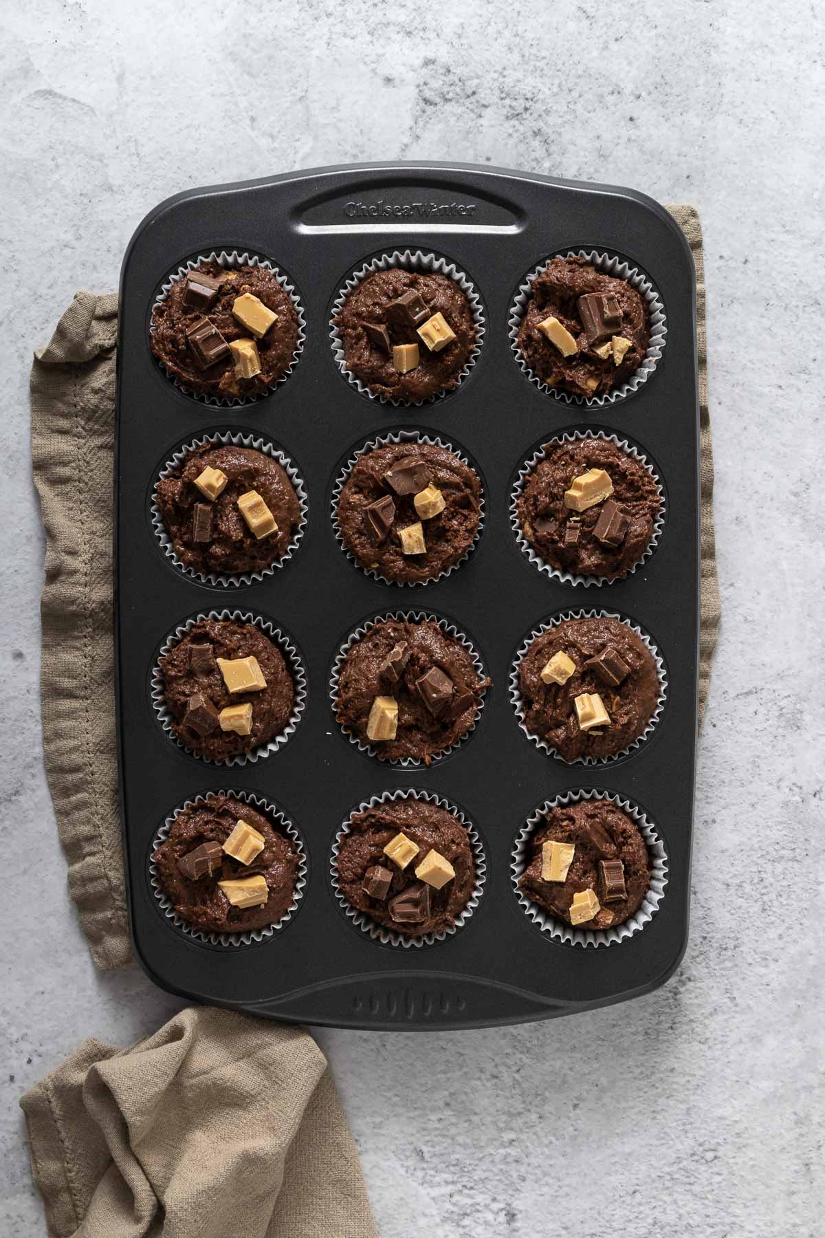 Chocolate Muffin Batter divided into 12 cupcake liners and topped with chocolate chunks.
