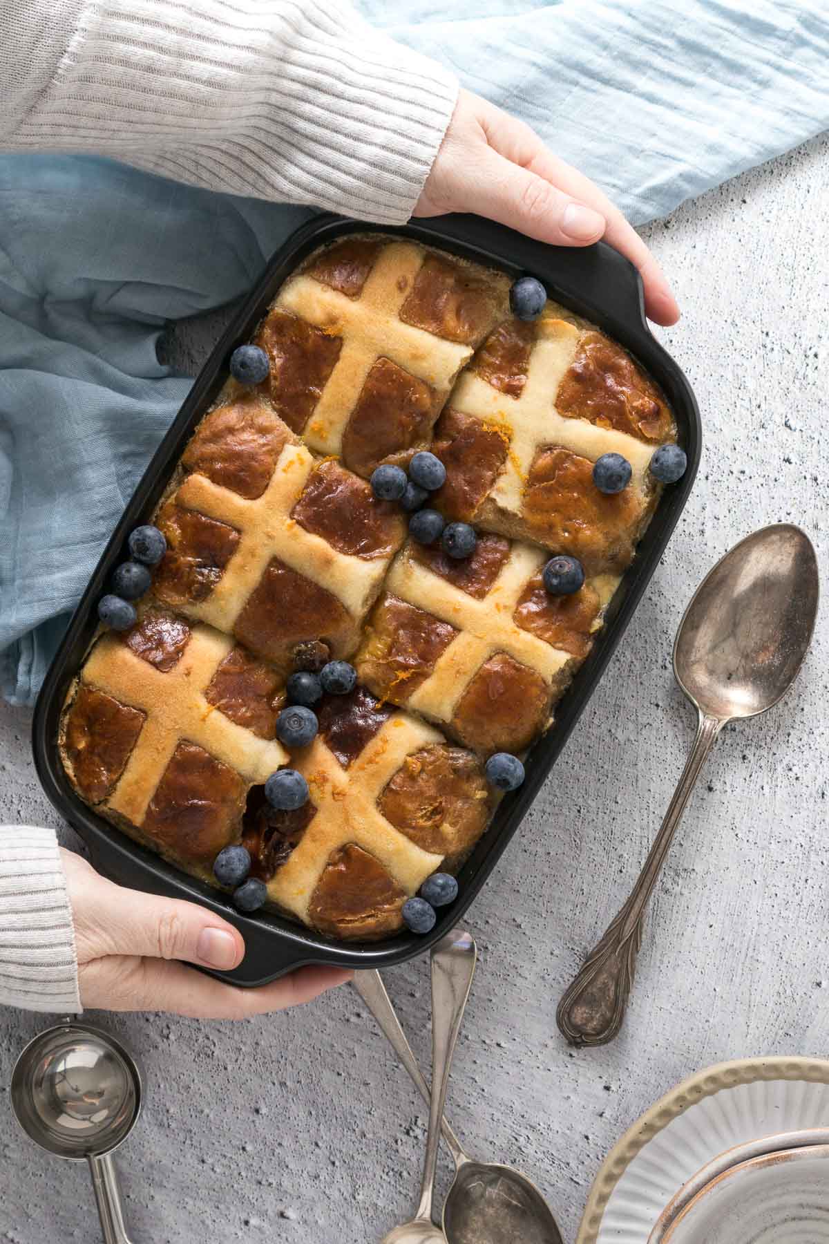 Baked hot cross bun pudding with fresh blueberries being placed on a table.