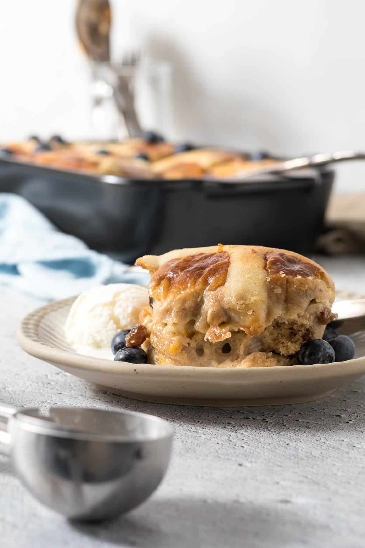 Serving of hot cross bun pudding on a plate with ice-cream.