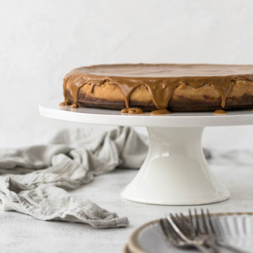 Biscoff cheesecake on cake stand with glaze dripping over the side.