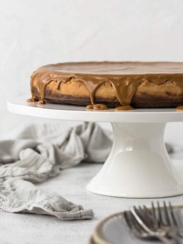 Biscoff cheesecake on cake stand with glaze dripping over the side.