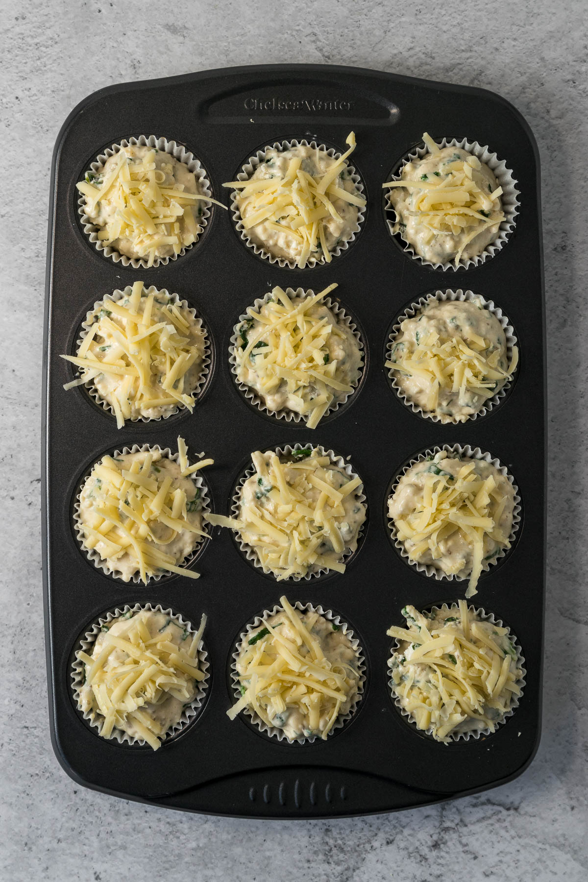 Muffin batter divided into liners and topped with cheese.