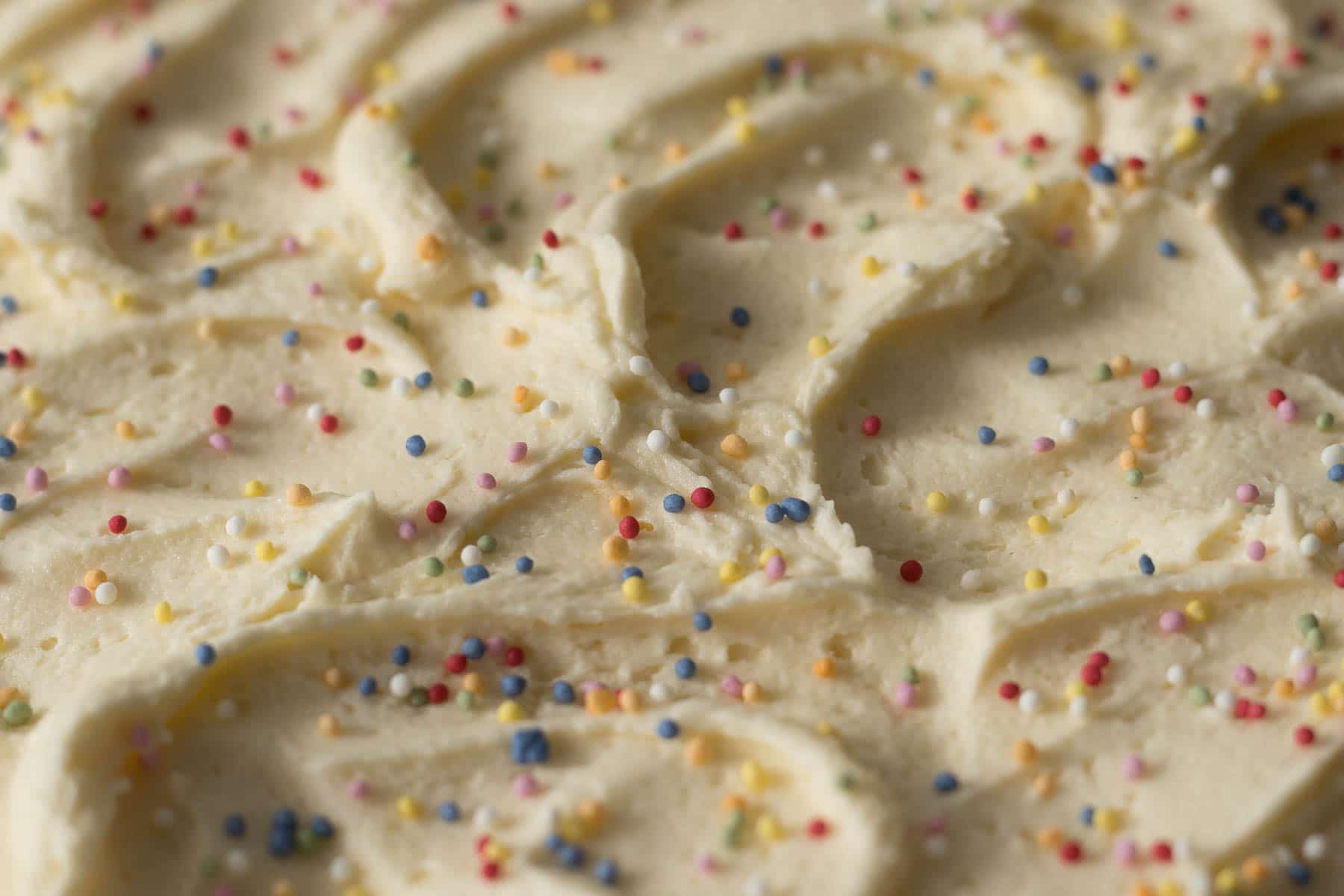Close up of vanilla buttercream frosting swirled on top of tray bake with sprinkles.