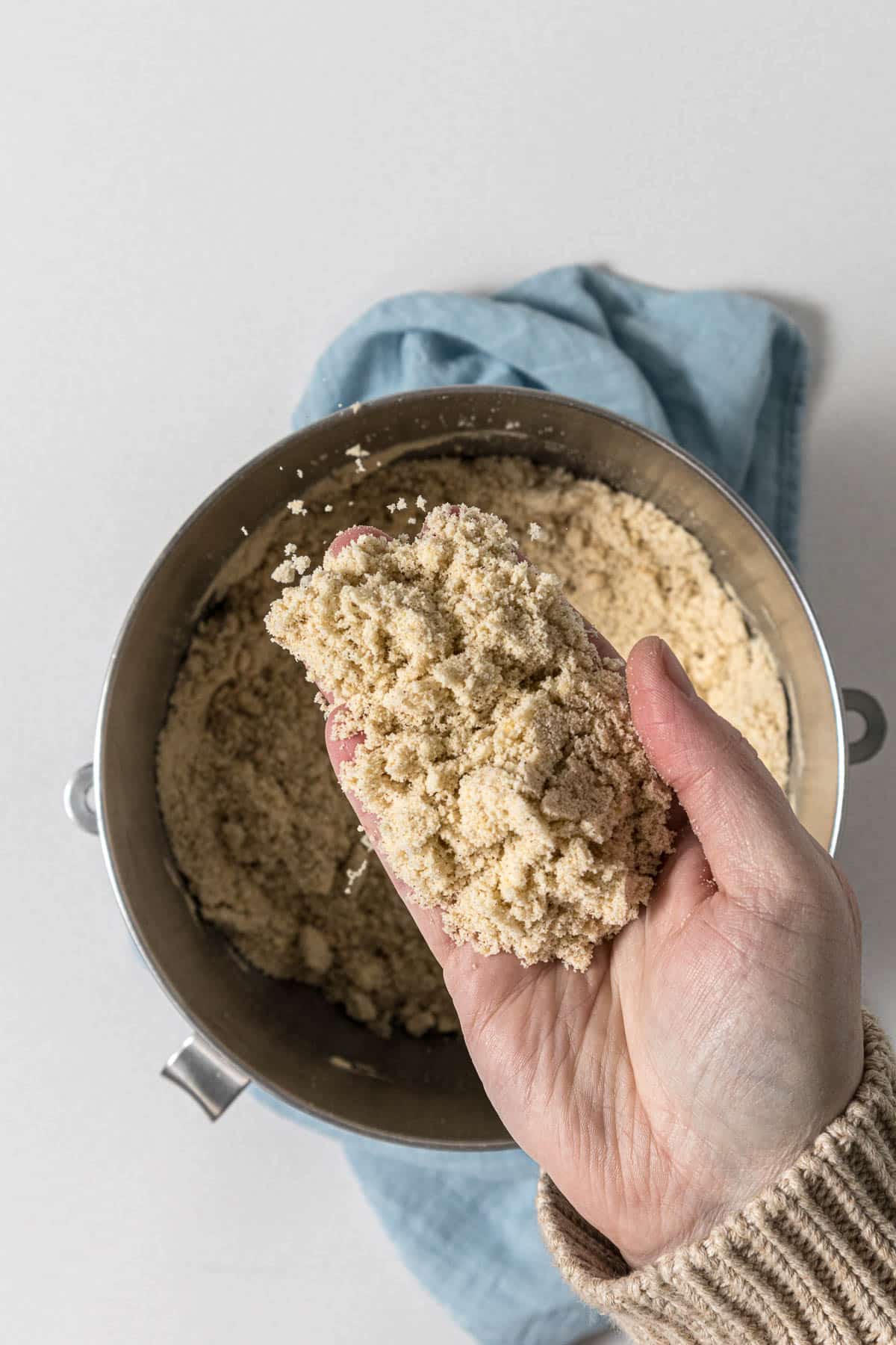 Step 2 - Hand holding up the butter-flour mixture to show the fine crumbs - wet sand texture.