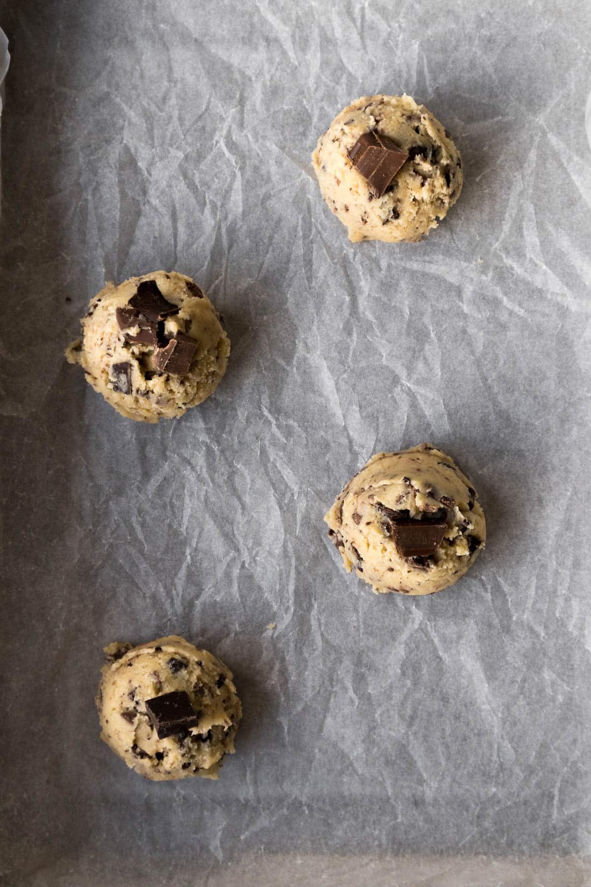 Scoops of cookie dough on a baking sheet dotted with chocolate chunks.