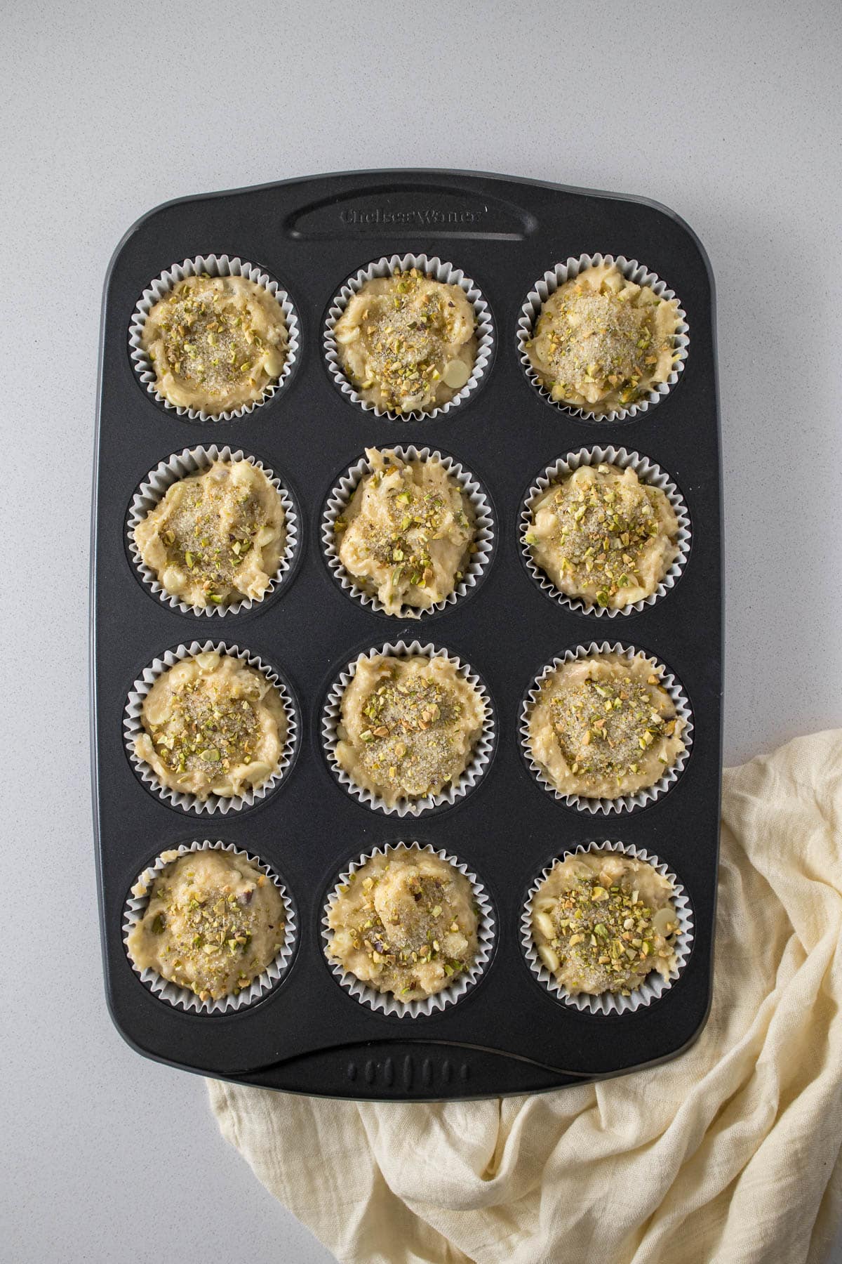 Pistachio muffin batter divided into 12 muffin liners.
