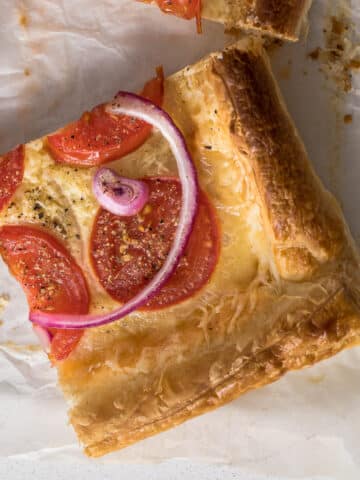 Sliced tomato puff pastry tart showing cheese, tomatoes and red onion.