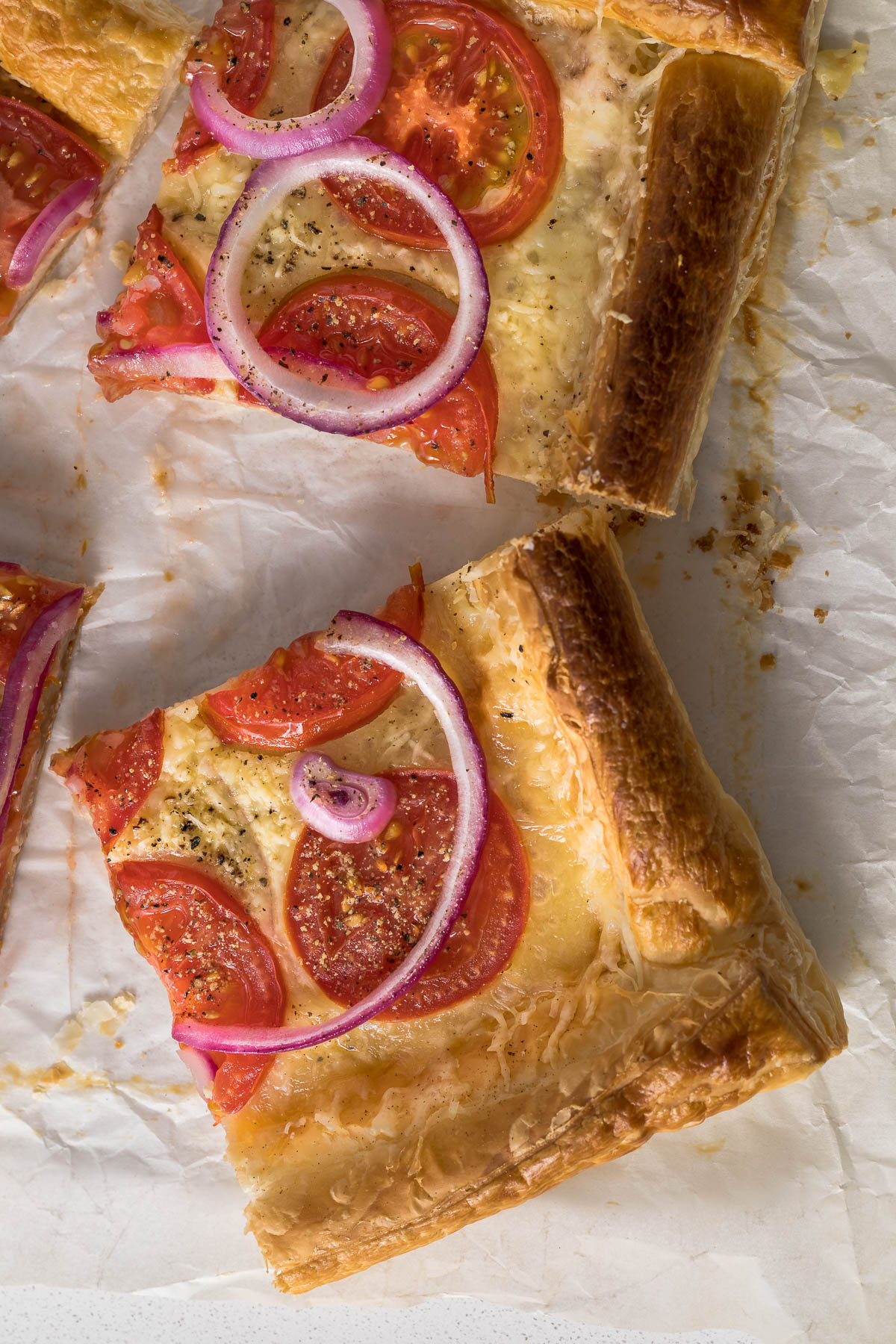 Sliced tomato puff pastry tart showing cheese, tomatoes and red onion.