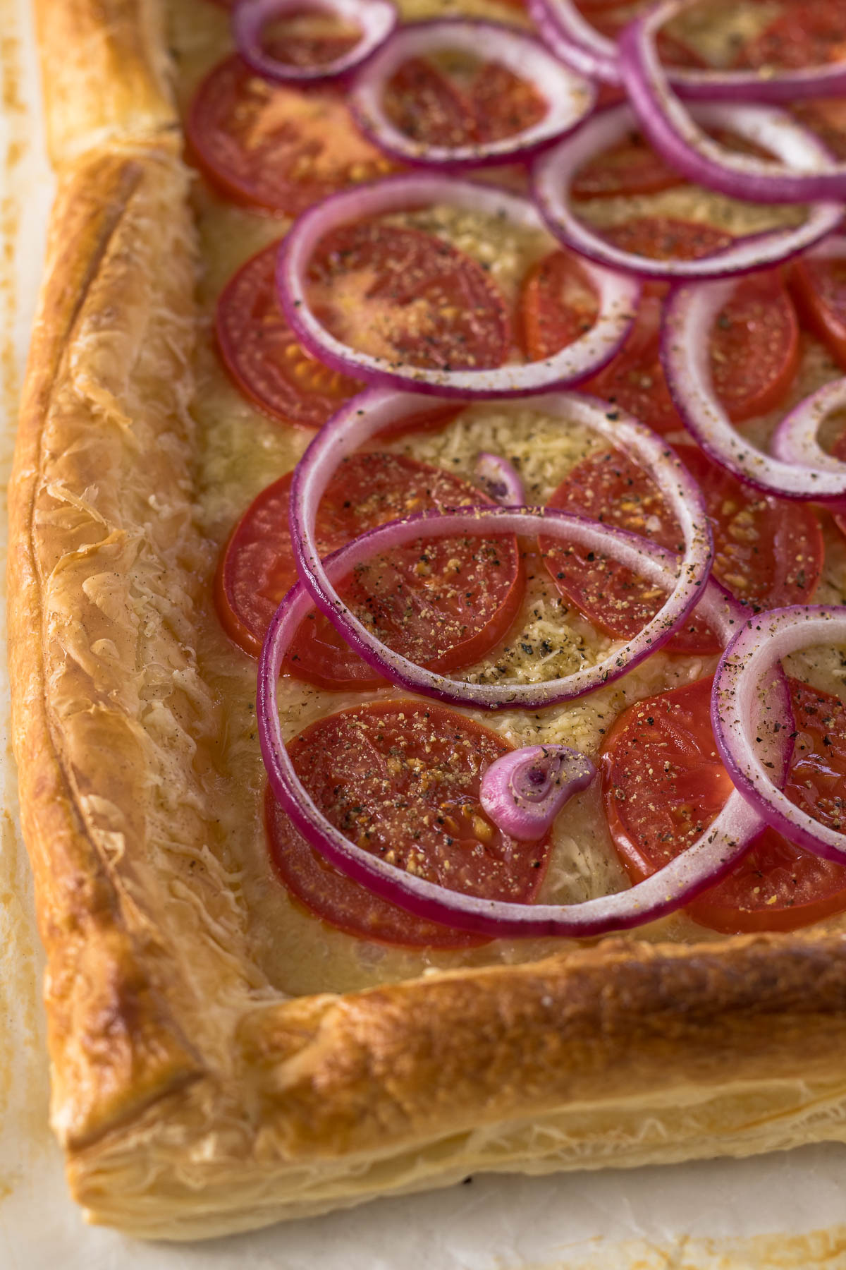 Close up of a tomato puff pastry tart showing tomatoes, cheese, and onions on a puff pastry base.