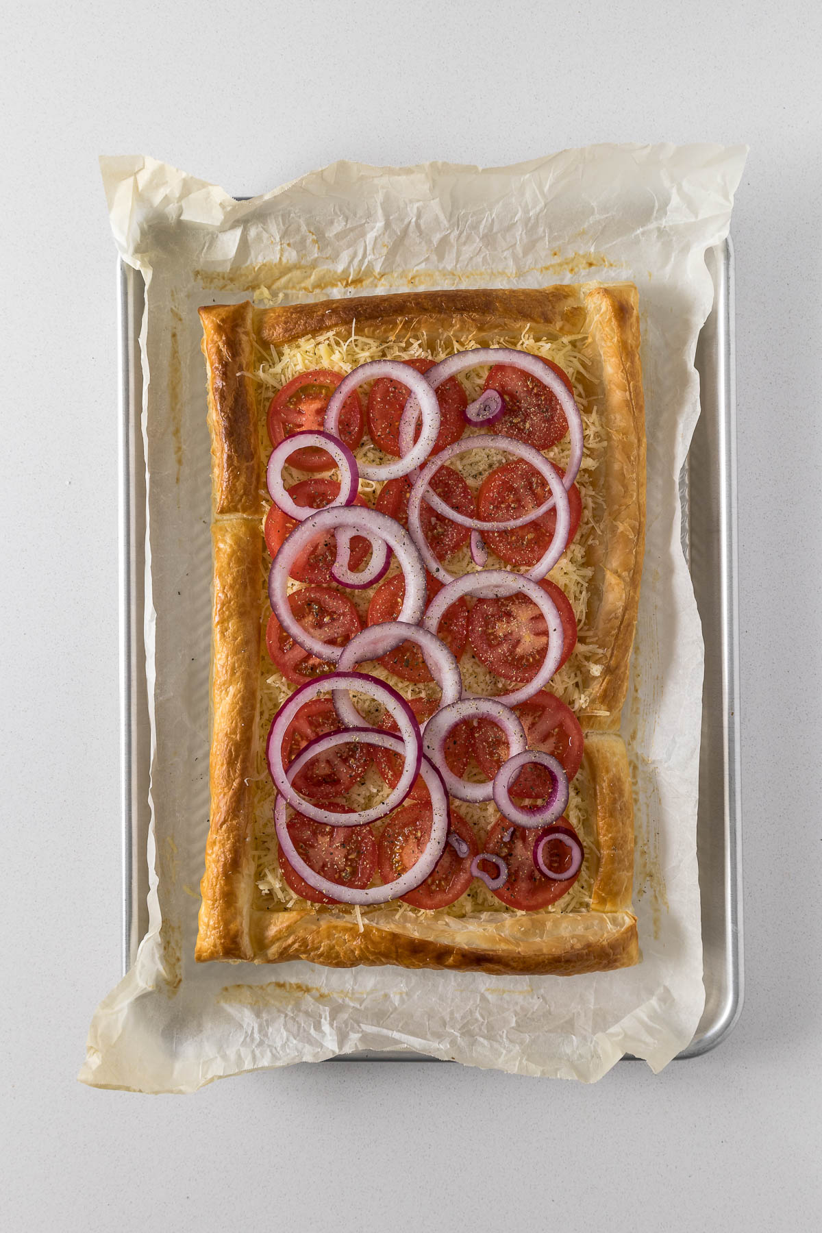 Step 11 - parbaked puff pastry topped with cheese, tomatoes and red onion.