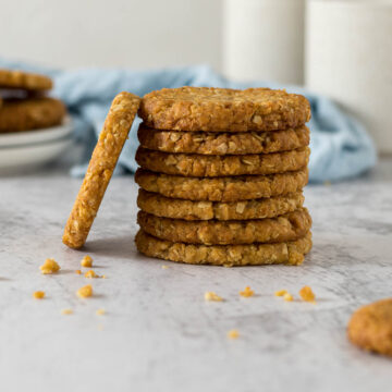 Stack of ANZAC biscuits with one propped on the side of the stack to show the side view.