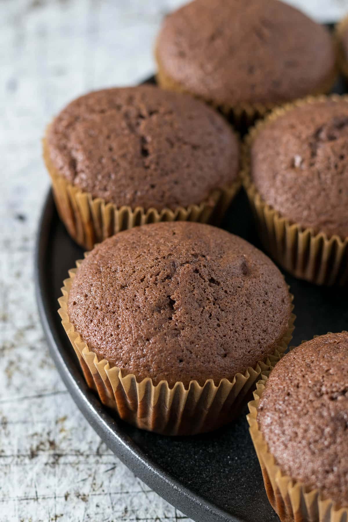 Baked, unfrosted chocolate cupcakes on a plate.