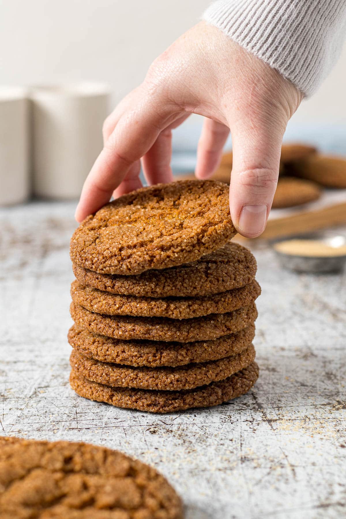 Hand picking up a ginger cookie off of a stack of cookies.