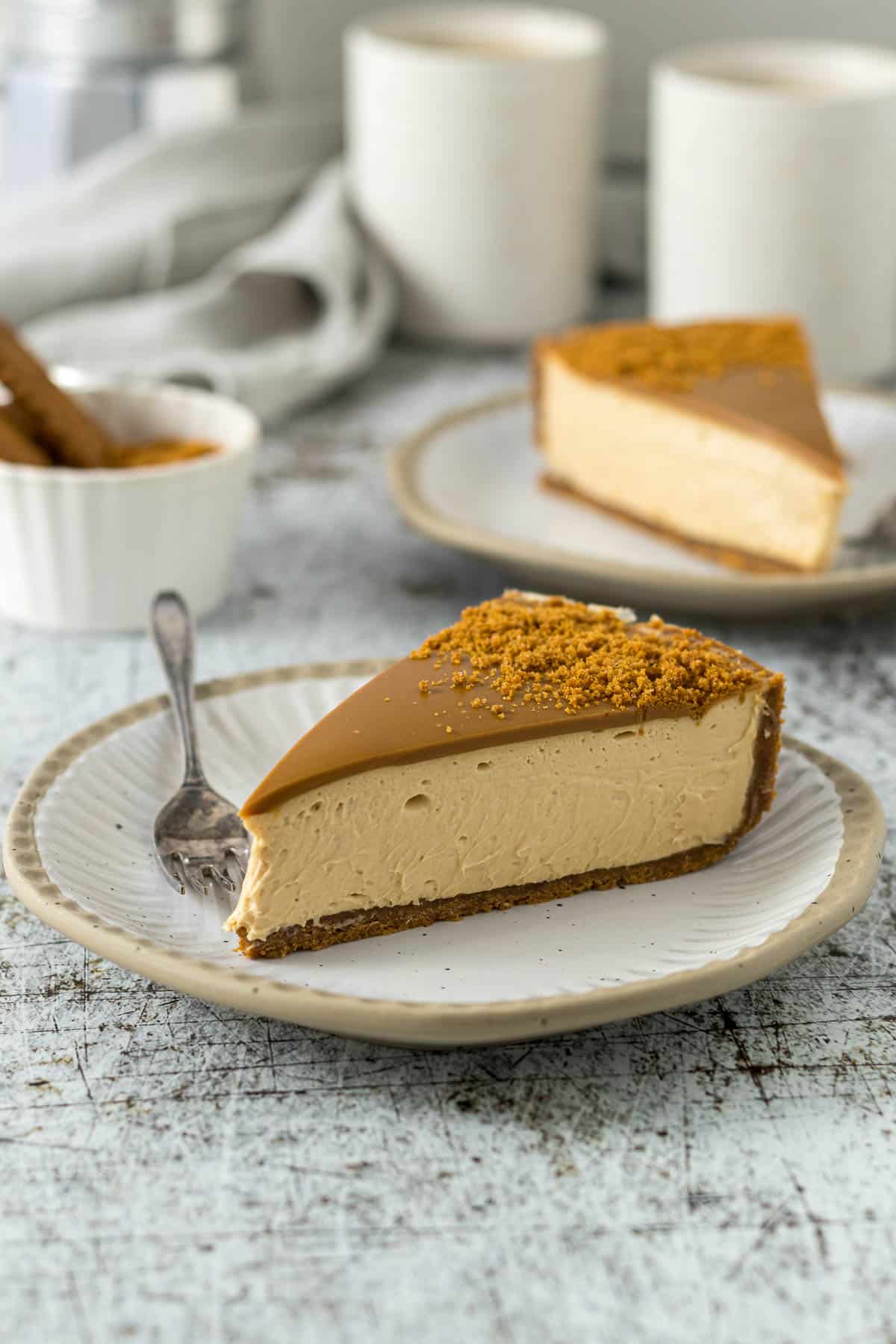 A slice of Biscoff cheesecake on a plate showing the layers of biscuit crust, cheesecake filling, and Biscoff spread topping.