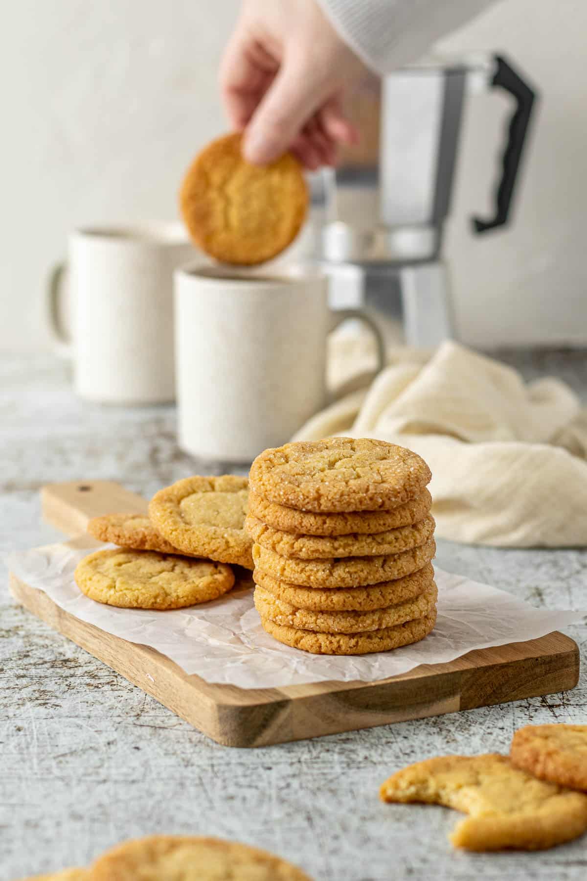 Vanilla cookies stacked on each other, with a cookie being dipped into coffee in the background.