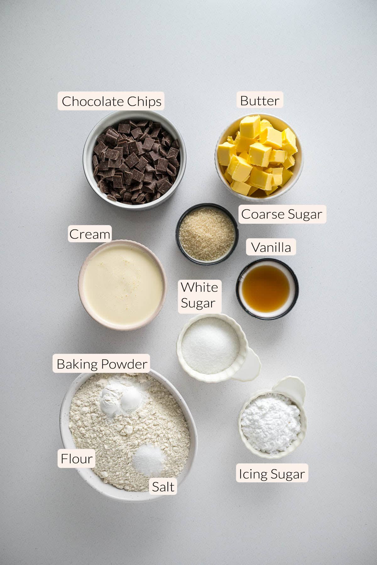 Chocolate chip scones ingredients - chocolate chips, butter, cream, coarse sugar, vanilla, white sugar, baking powder, flour, salt, and icing sugar.