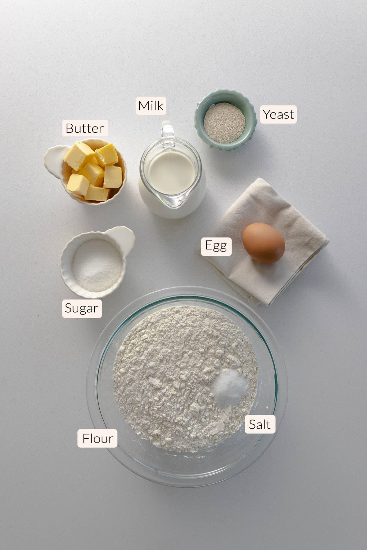 Bread dough ingredients - flour, salt, sugar, butter, milk, an egg, and active yeast.
