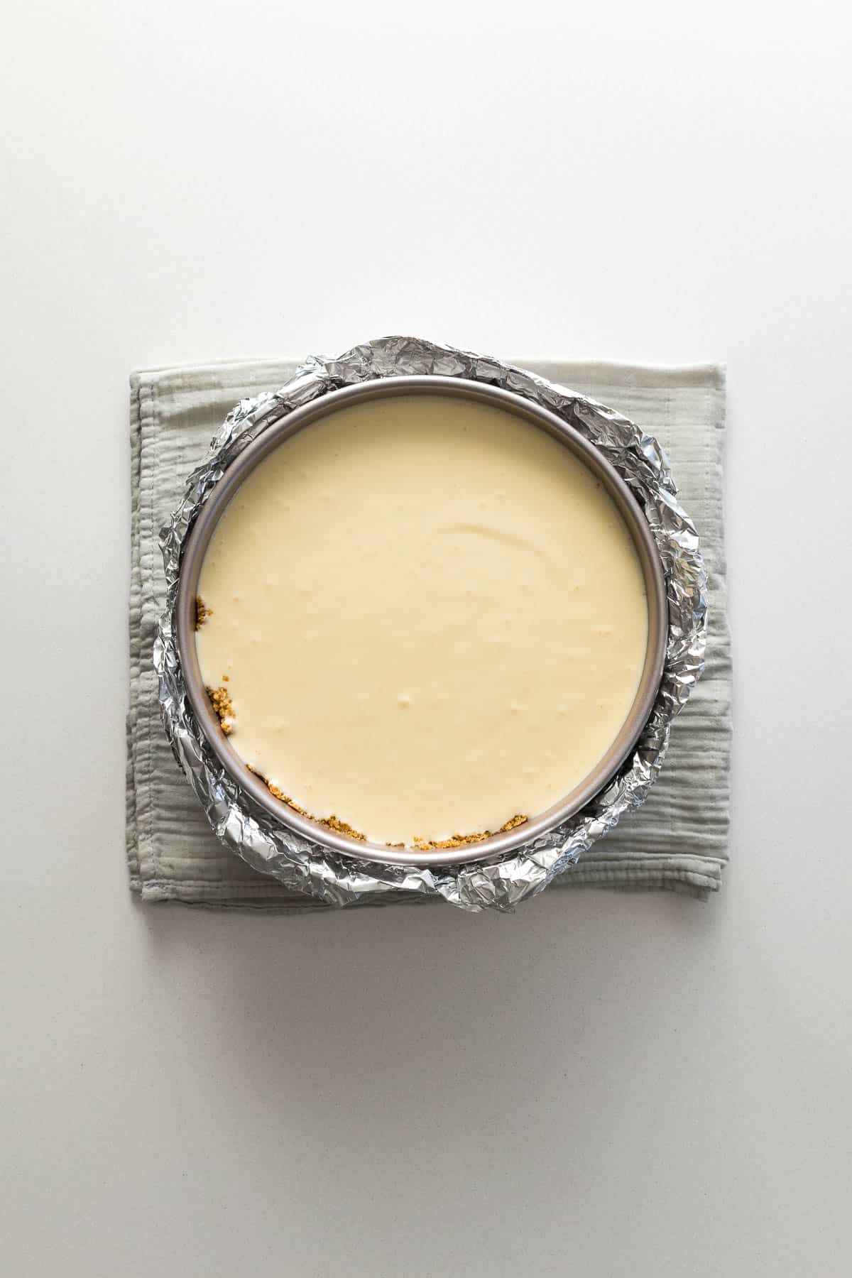 Step 10 - Cheesecake batter poured into the baked biscuit base, with the pan wrapped in foil.