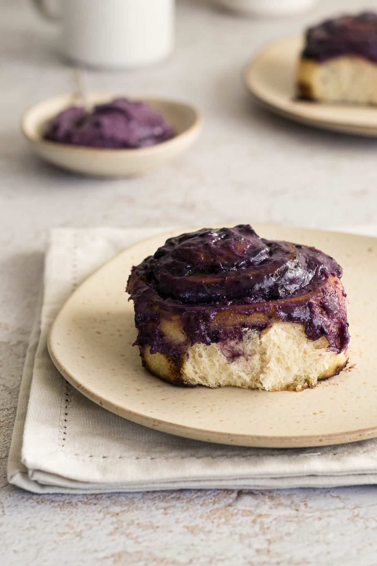 Cinnamon blueberry rolls on a plate topped with a blueberry cream cheese frosting.