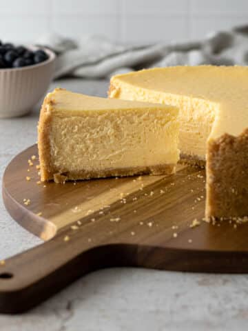 Slice of cheesecake next to the full cheesecake on a serving board.