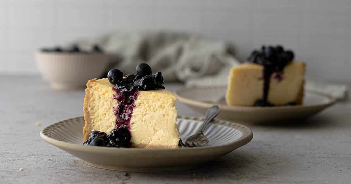 Slices of New York cheesecake on plates with a blueberry topping.