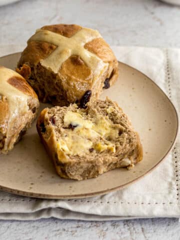 Hot cross buns sliced on a plate with some butter.