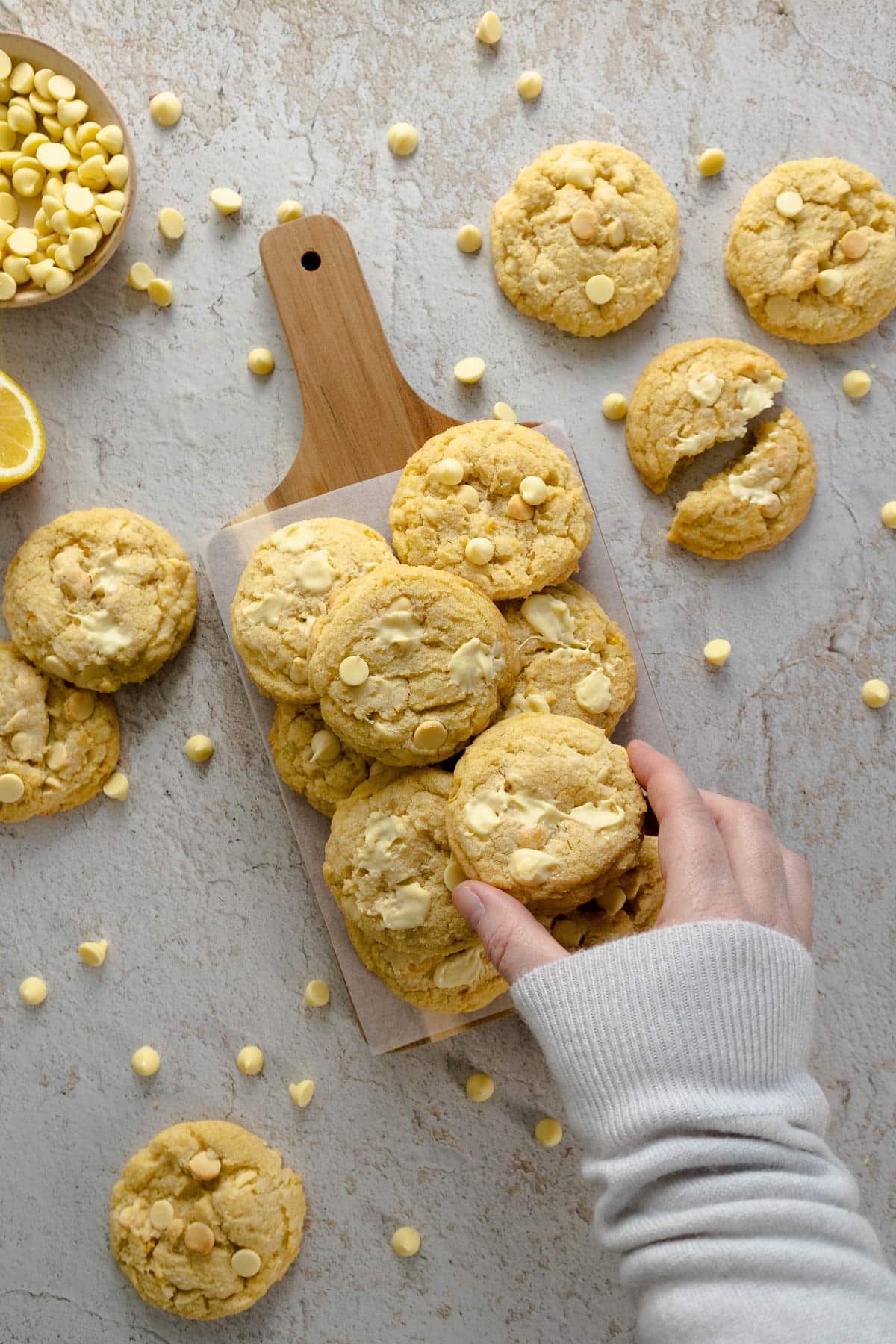 Lemon white chocolate cookies arranged on a platter with a hand picking up a cookie.