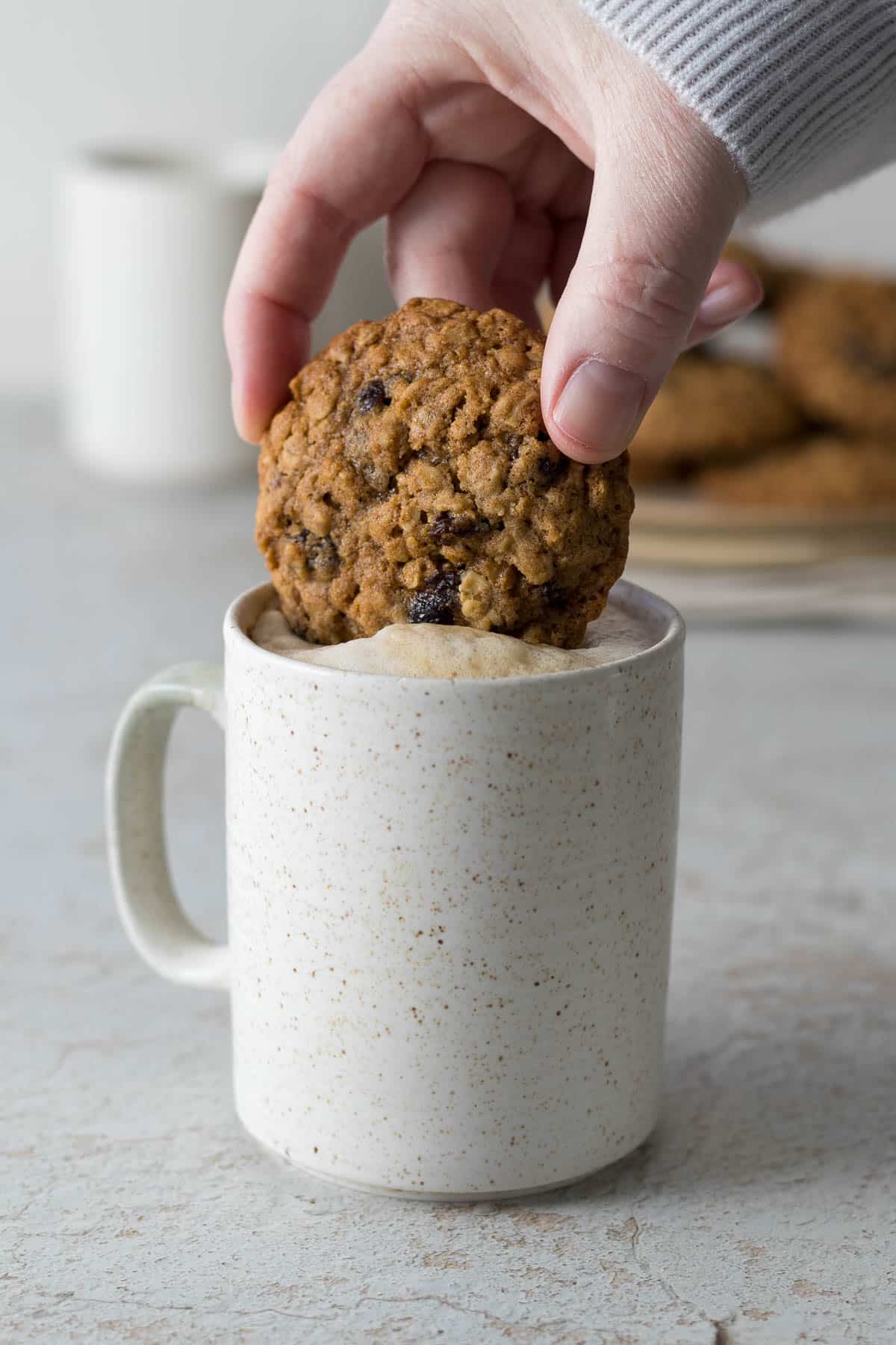 A hand dipping an oatmeal cookie with raisins into a cup of coffee.